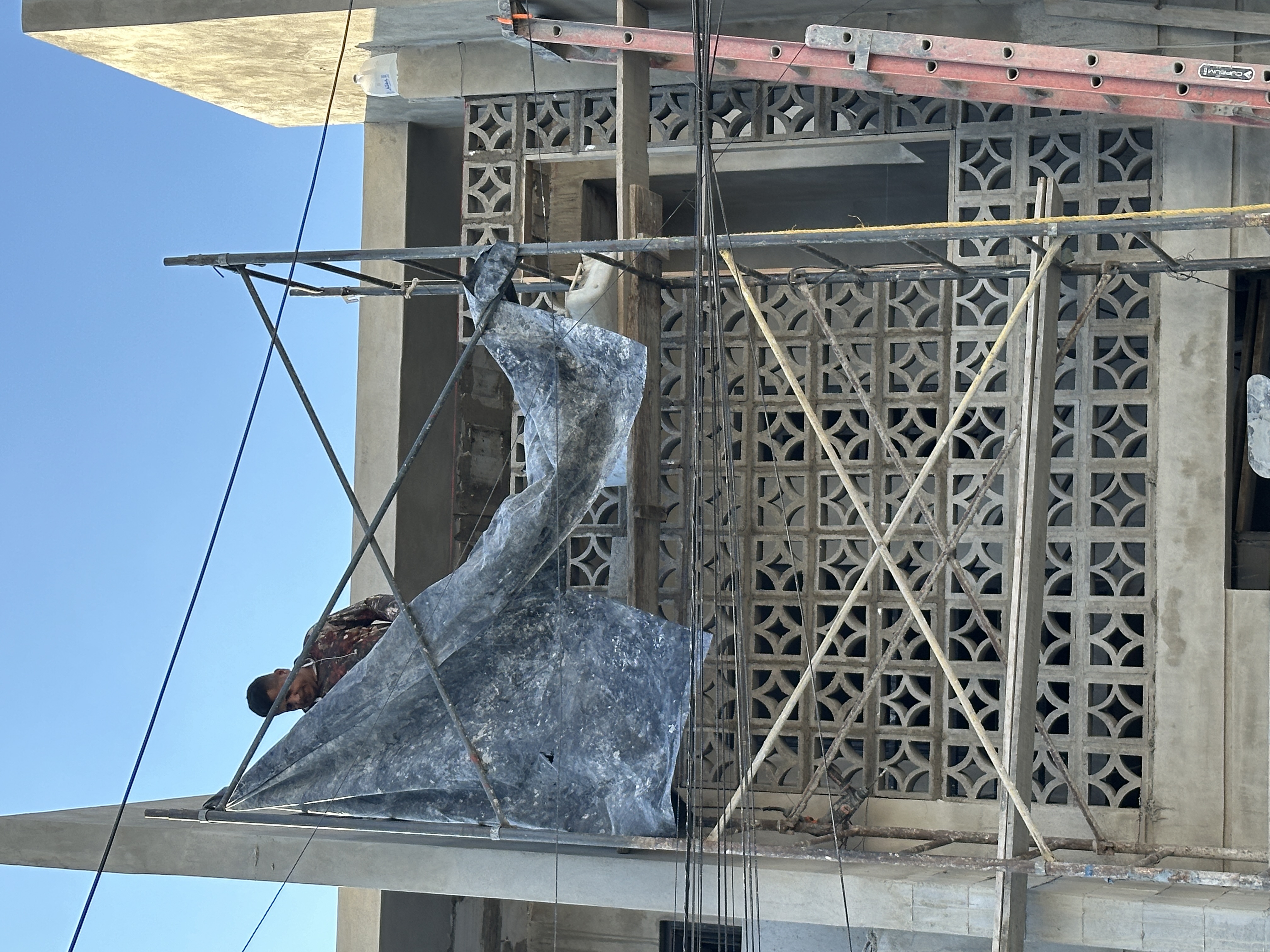 Instalación de la celosía artesanal de concreto — trabajadores sobre andamio frente al patrón geométrico