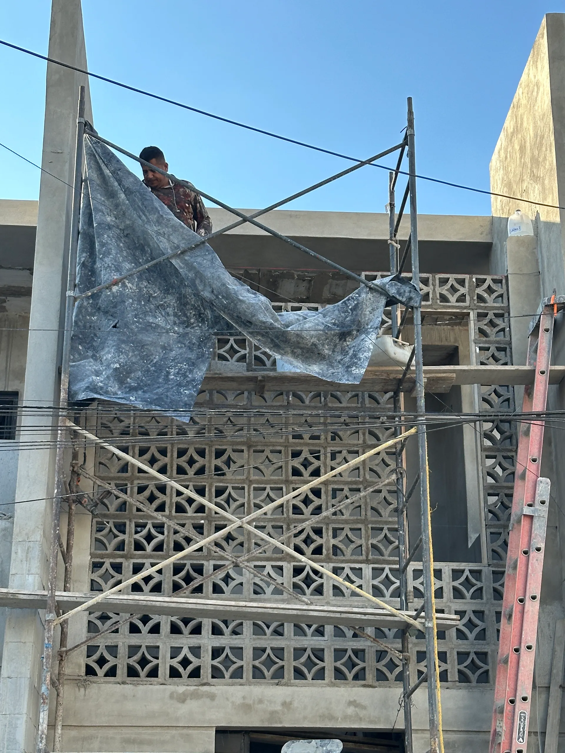 Instalación de la celosía artesanal de concreto — trabajadores sobre andamio frente al patrón geométrico