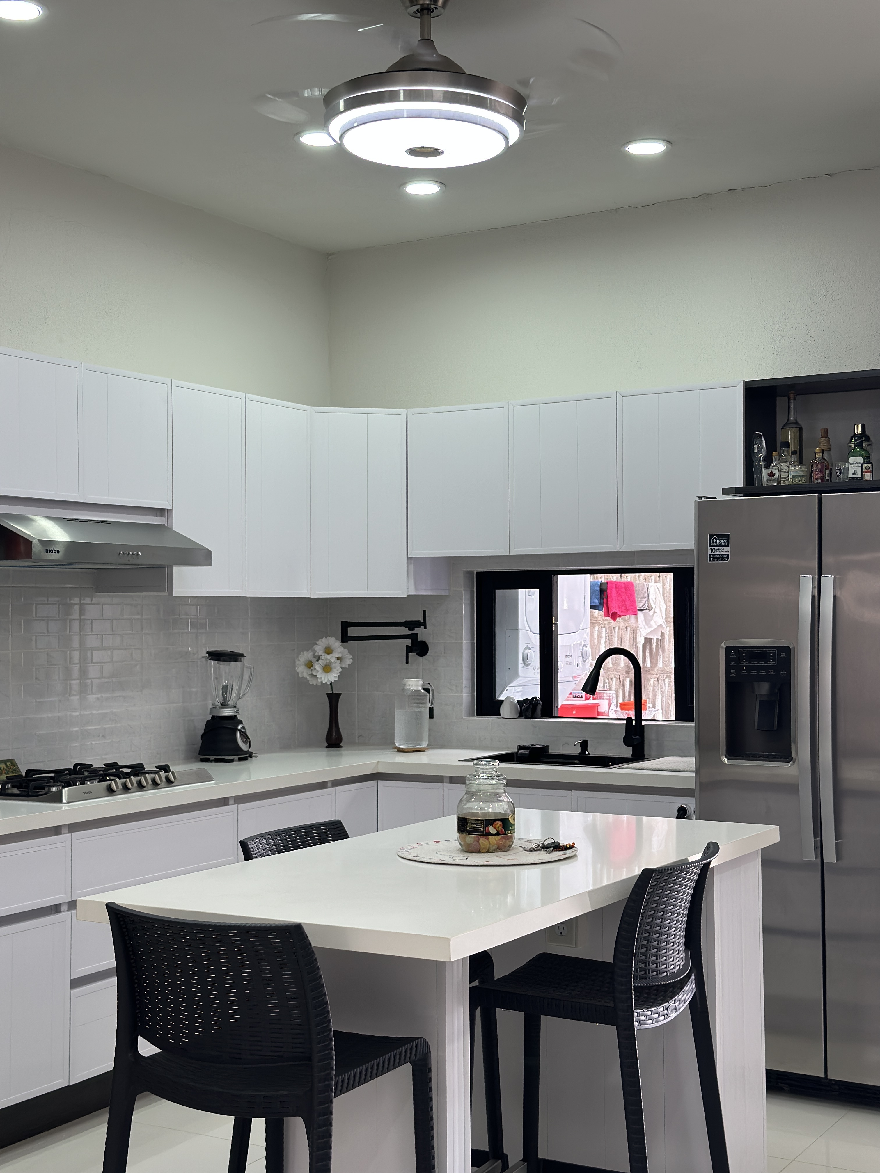 Cocina segundo nivel — gabinetes blancos con isla y sillas bar negras — Casa Manglar