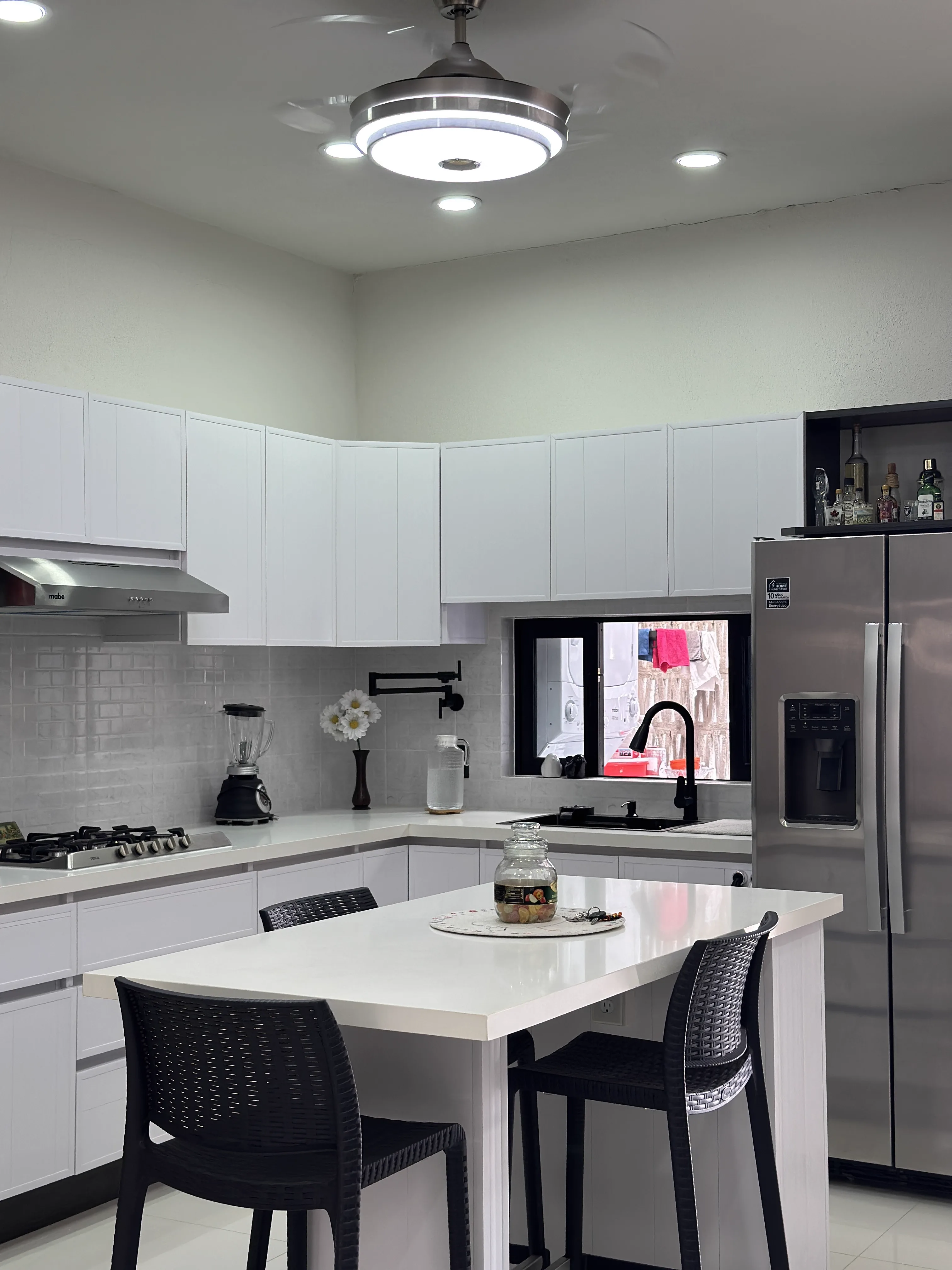 Cocina segundo nivel — gabinetes blancos con isla y sillas bar negras — Casa Manglar