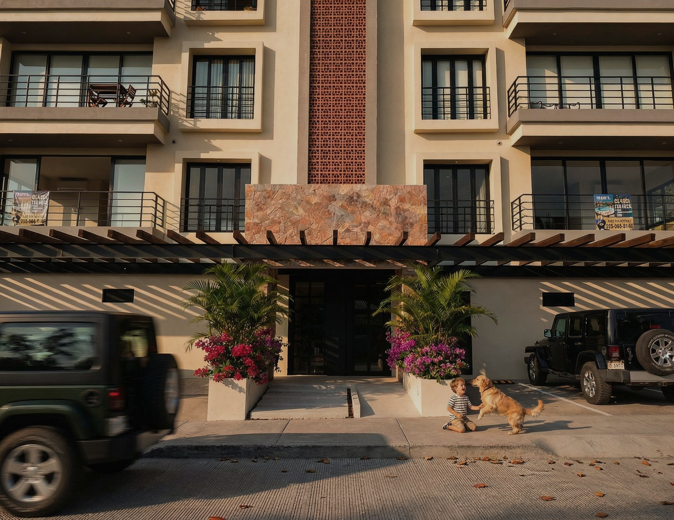 Entrada del edificio ZUL PV — jardín con bugambilias, pérgola y lobby iluminado
