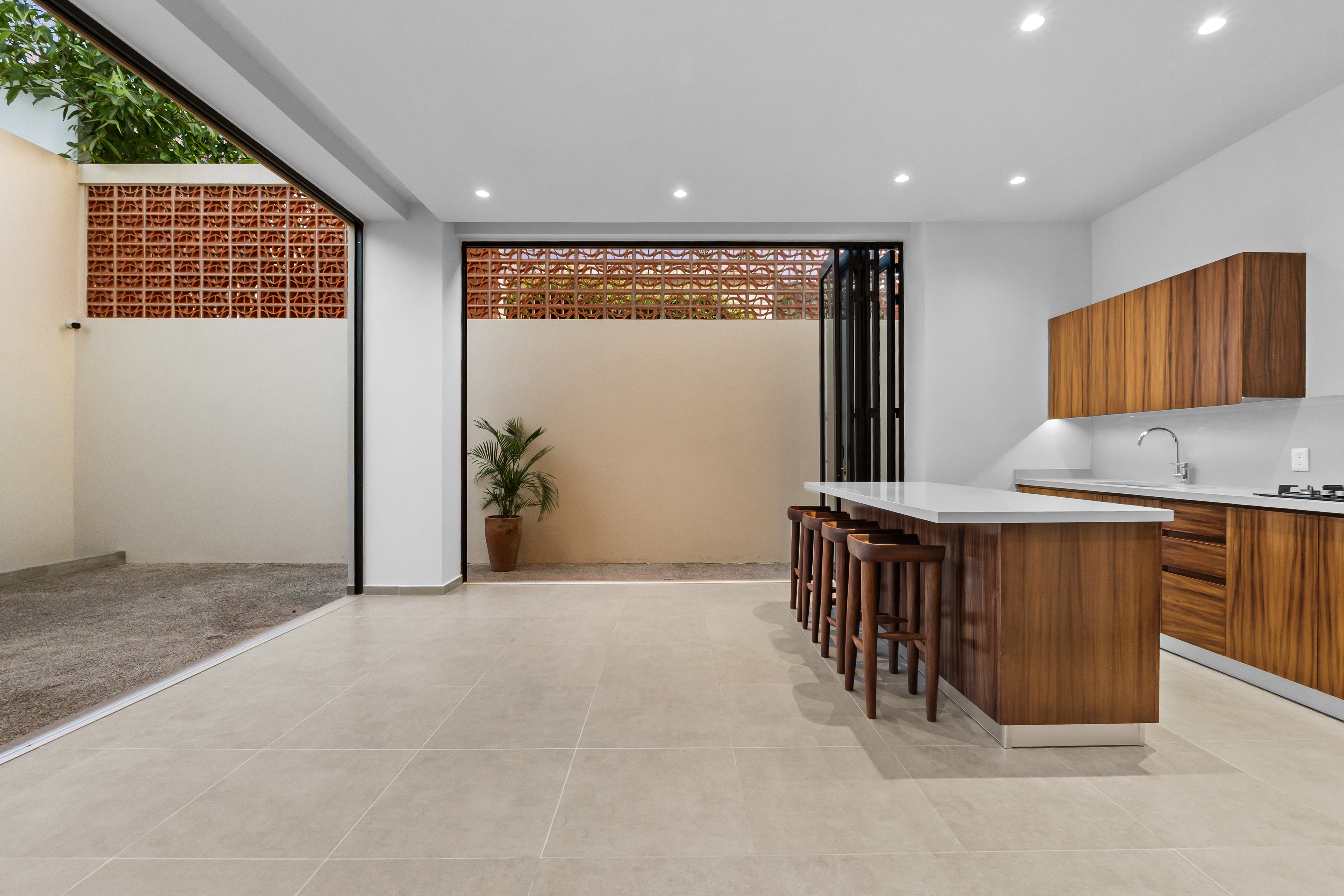 Cocina con isla de parota y cuarzo, puertas plegables al patio con celosía de ladrillo — ZUL PV