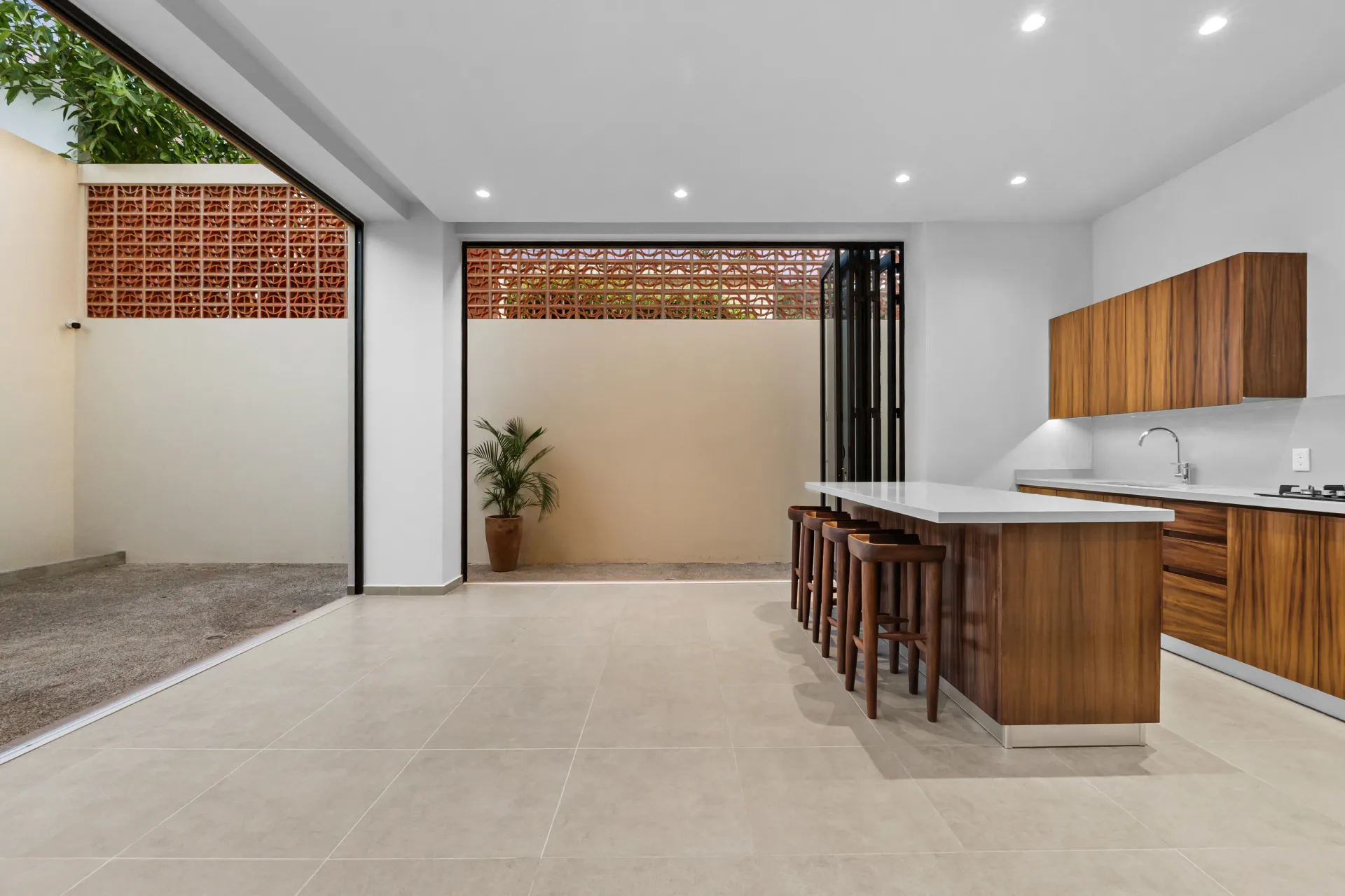 Cocina con isla de parota y cuarzo, puertas plegables al patio con celosía de ladrillo — ZUL PV